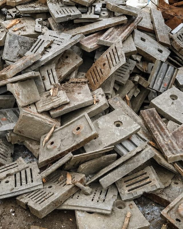 Cast metal machine parts and plates piled on a scrapyard floor.