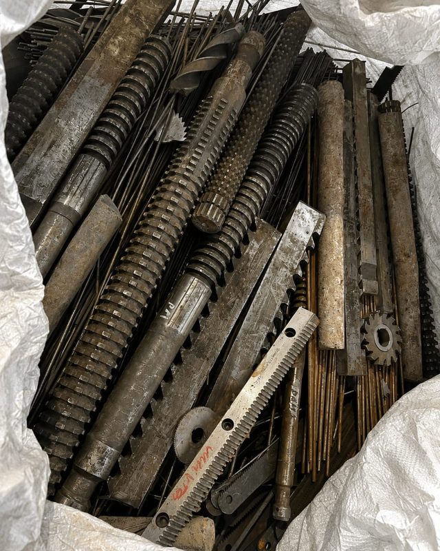 Machined steel shafts, screws and gears collected in a bulk bag.