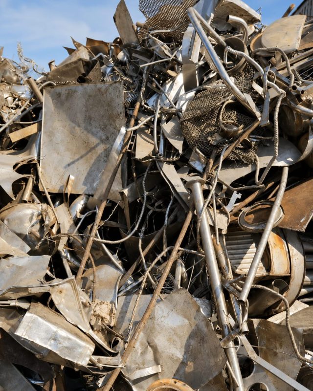 A mixed metal scrap pile of sheet offcuts, wire and cable under open sky.